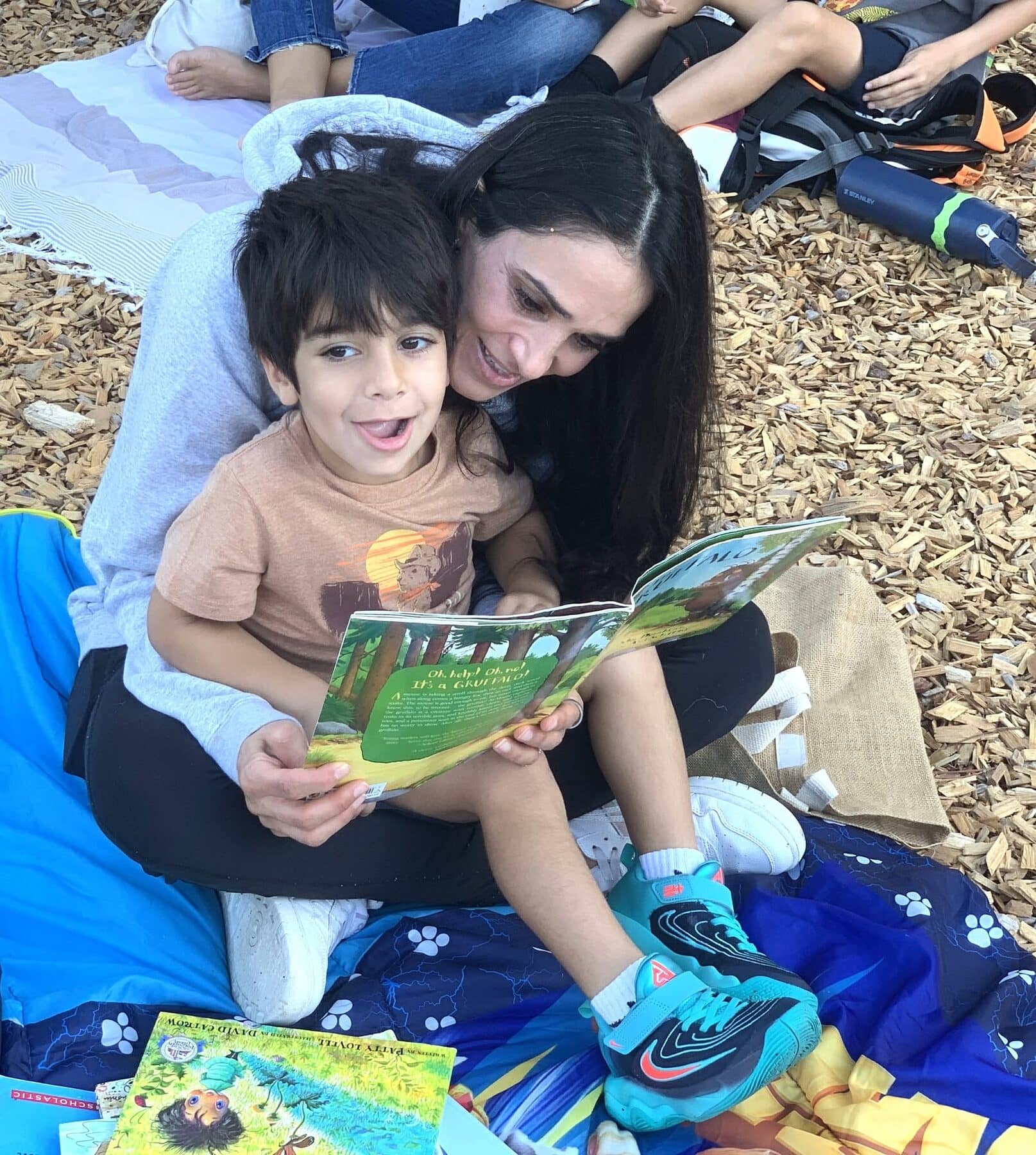 An adult reading with a young child outdoors.