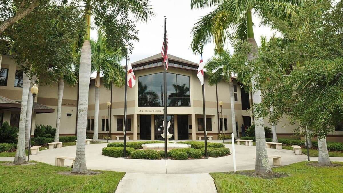 The Saint Stephen's campus building entrance with U.S. and Florida flags framed by palm trees.