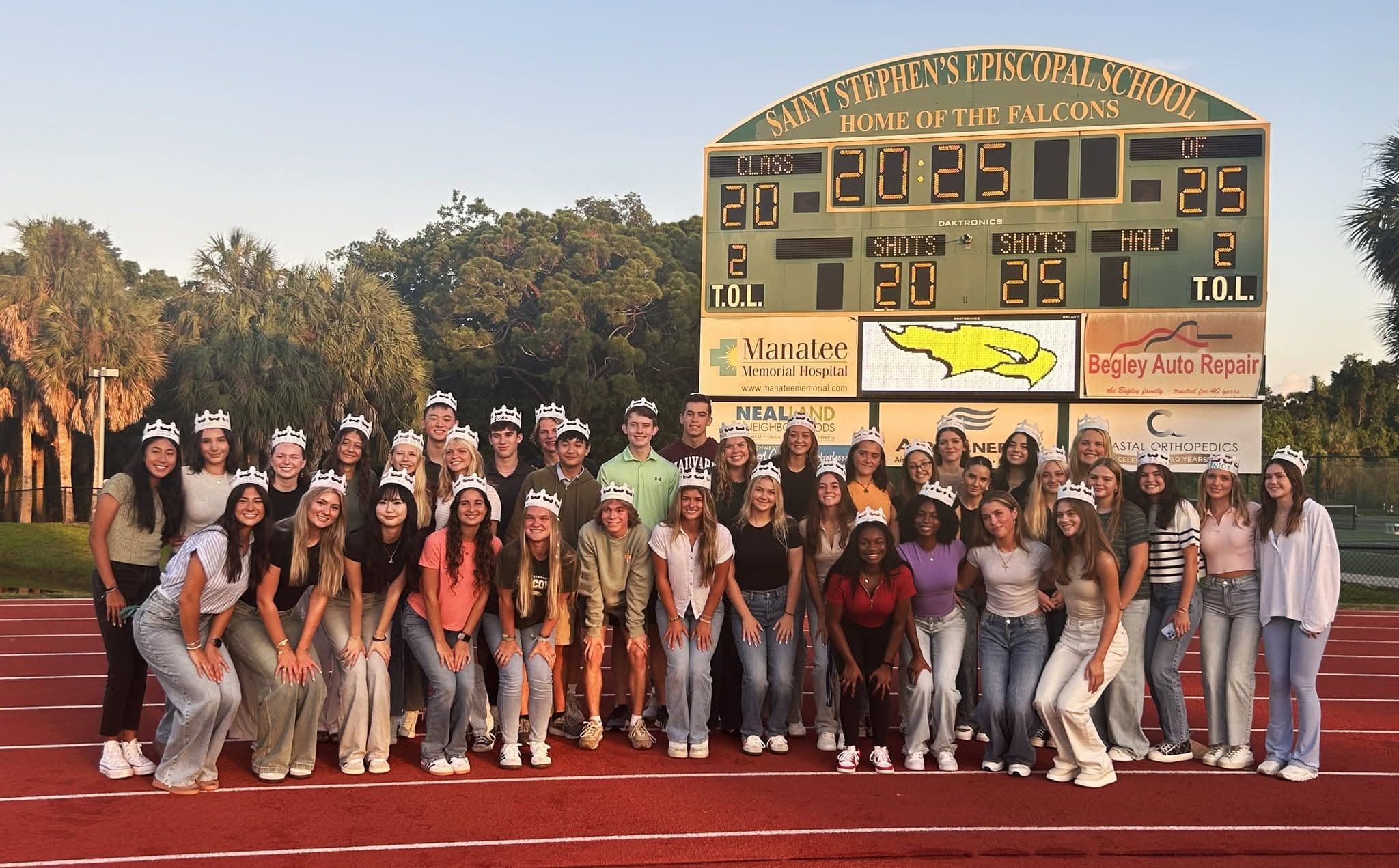 Saint Stephen's students in paper crowns gathered on the track in front of the Falcons stadium scoreboard