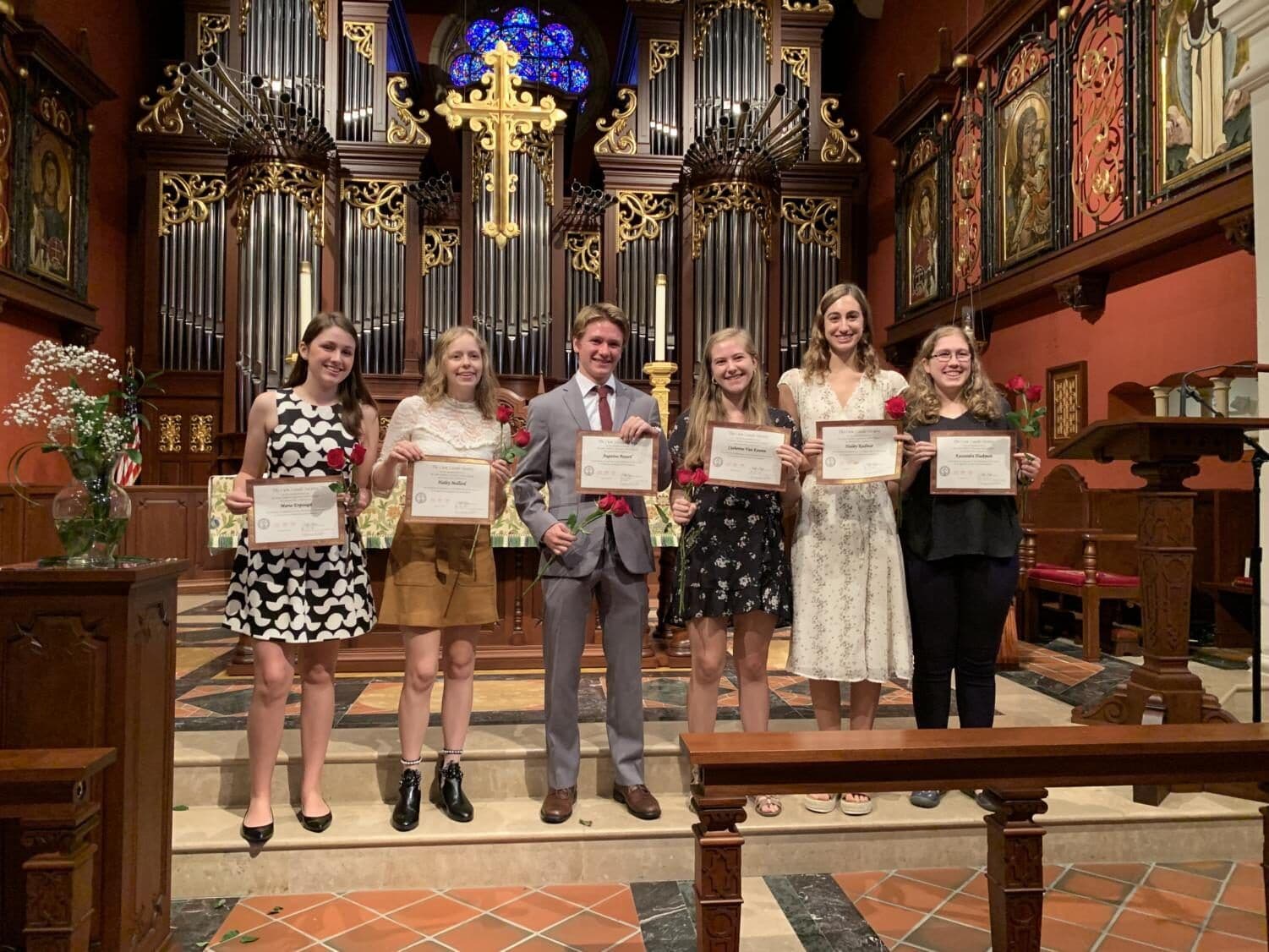 Students hold award certificates in the chapel in front of the organ pipes and altar.