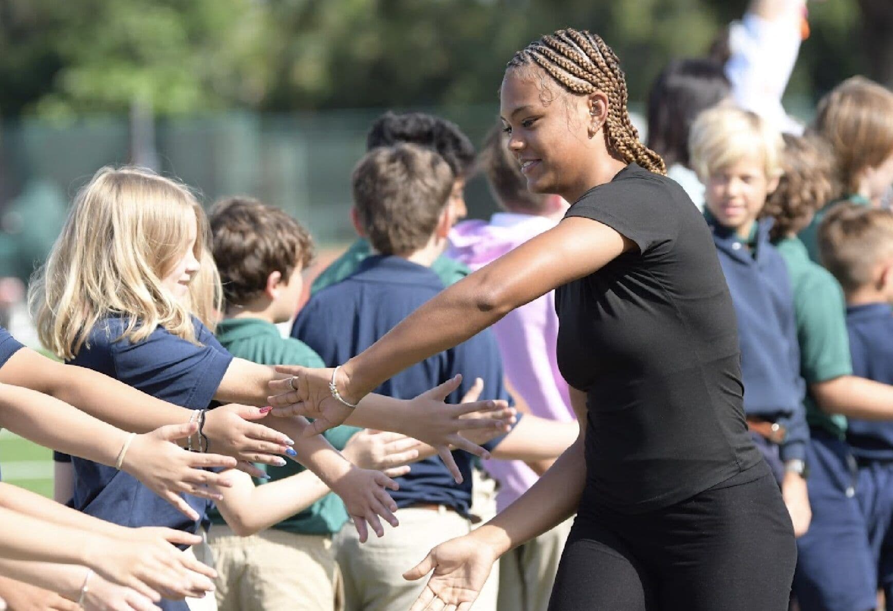 An athlete high-fives a tunnel of cheering younger students during a team send-off.