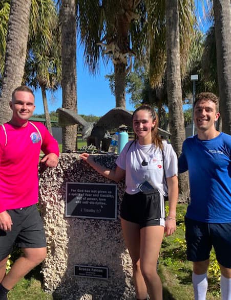 Three alumni posing with the bronze falcon statue